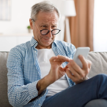 Mature man squinting using mobile phone, looking at screen