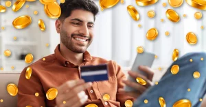 Smiling man using phone and credit card at home - Golden Coins Rain 3D